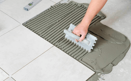 a hand using a trowel on a tile floor